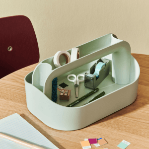 Recycled tool box organizer with office supplies: tape, scissors, pencils, sharpener, and color swatches on a wooden desk.