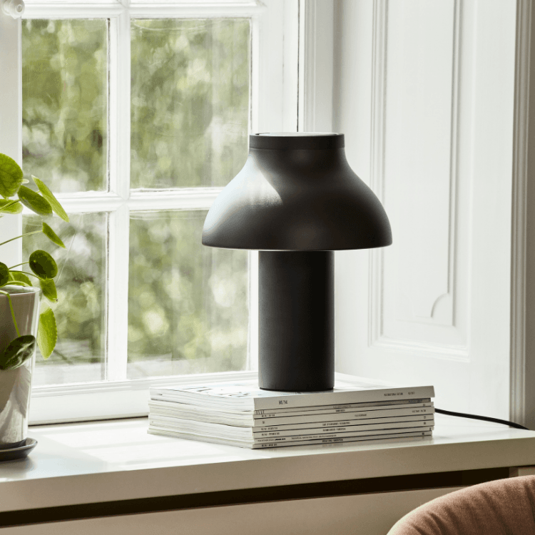Modern black PC table lamp on books by a window, stylish home decor lighting solution, ambient light.