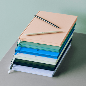 Stack of colourful HAY notebooks with pens, perfect for journaling and note-taking. Stylish stationery for creative minds.