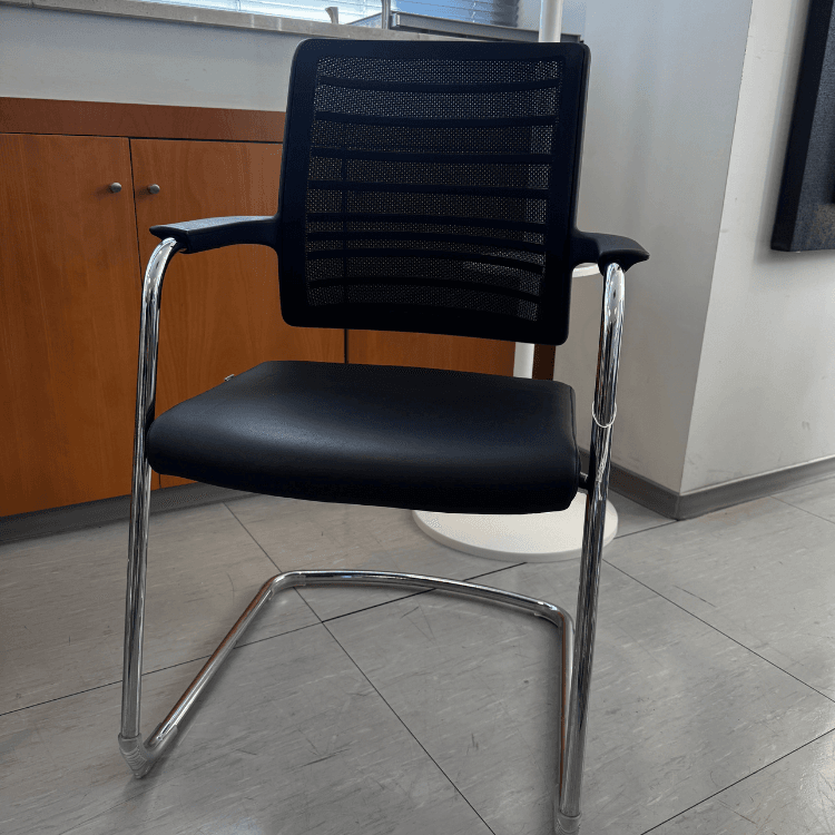 A black office chair with a mesh back and cantilevered chrome legs sits on a tiled floor.