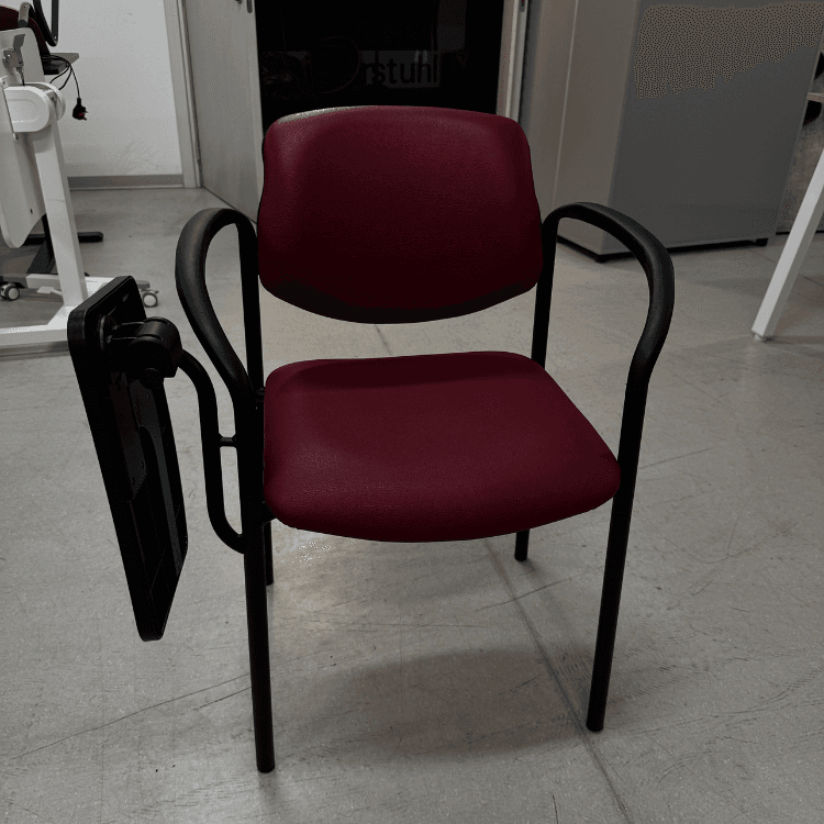 A maroon upholstered chair with black metal frame and attached black writing tablet is pictured indoors.