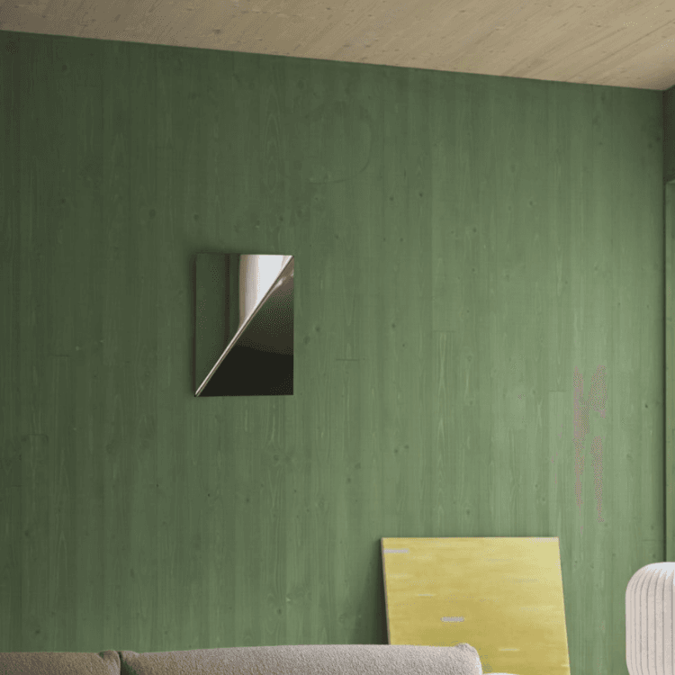A rectangular mirror hangs on a green wood-paneled wall above a sofa, with a yellow abstract painting leaning below it.