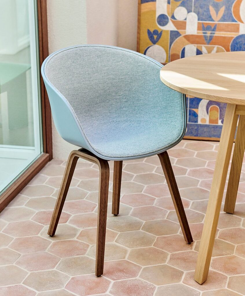 Light blue upholstered chair with wooden legs beside a wooden table on a tiled floor.