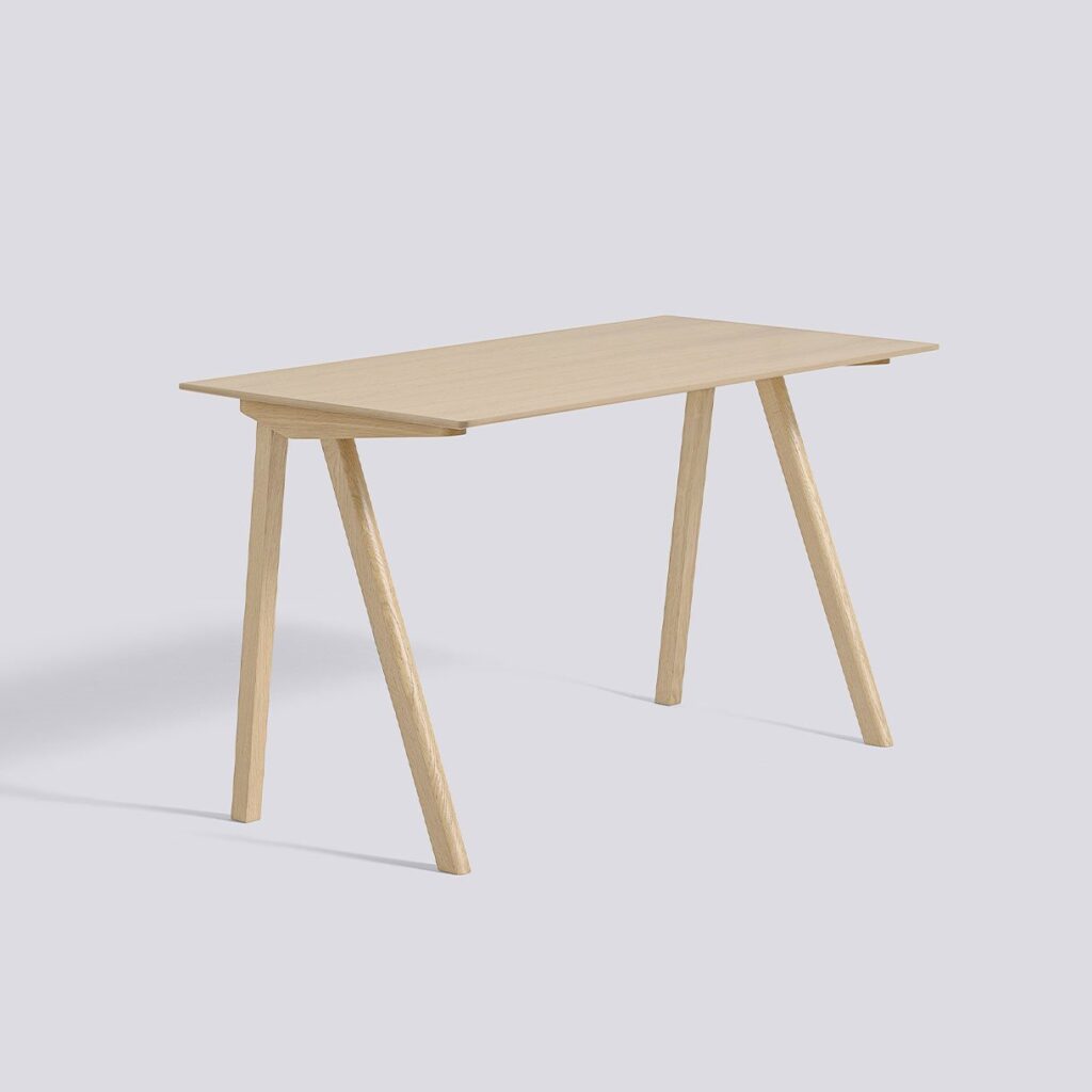 A light wood desk with a rectangular top and four splayed legs on a plain background.