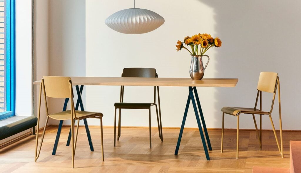 A rectangular wooden dining table with metal legs, surrounded by three chairs and a vase of sunflowers, under a white pendant lamp.