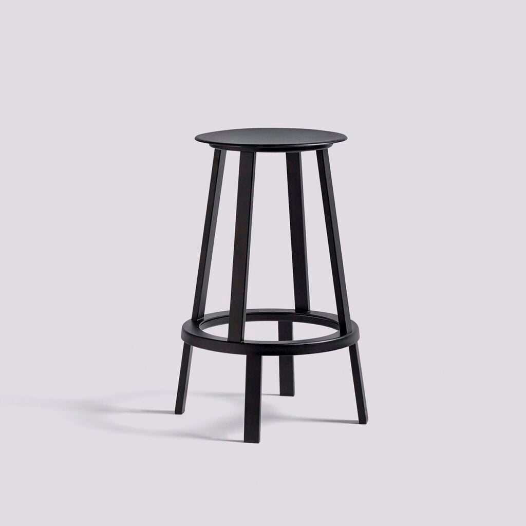A black wooden stool with a round seat, four tapered legs, and a circular footrest ring on a grey background.