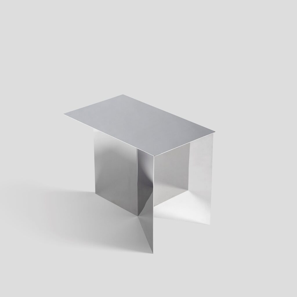 A rectangular table with a flat top and angular metal legs, standing on a plain light gray background.